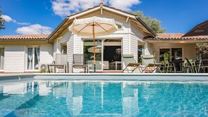 Una casa con piscina, mobiliario exterior y una sombrilla.