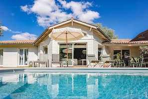 Ein Haus mit Swimmingpool, Gartenmöbeln und Sonnenschirm.