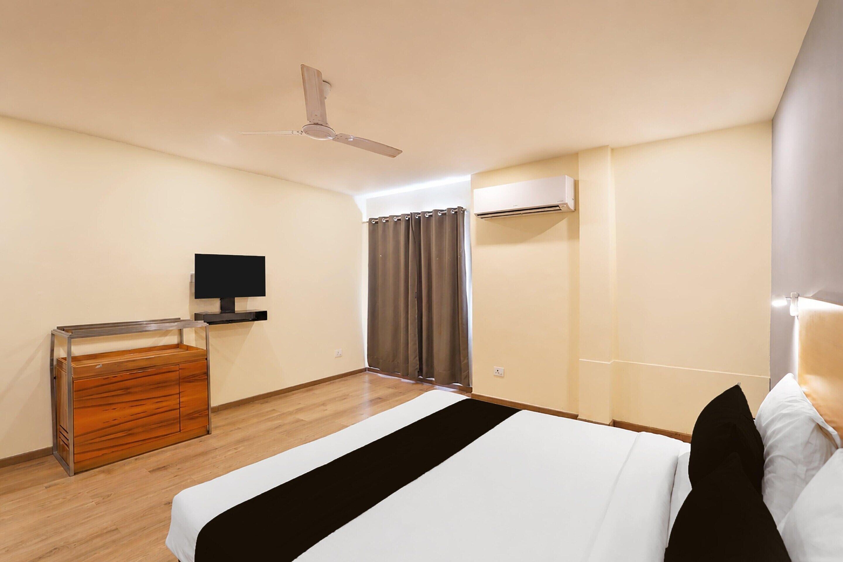 Habitación de hotel con cama, televisor, cómoda de madera, ventilador de techo y aire acondicionado.