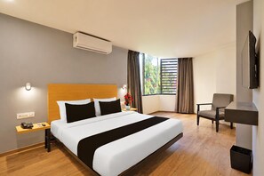 A hotel room with a large bed, a desk, a chair, an air conditioning unit, and a television.