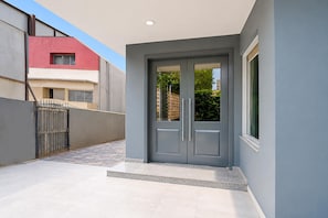 Un edificio moderno con una puerta gris, un ventanal pequeño, una verja metálica y un camino pavimentado.