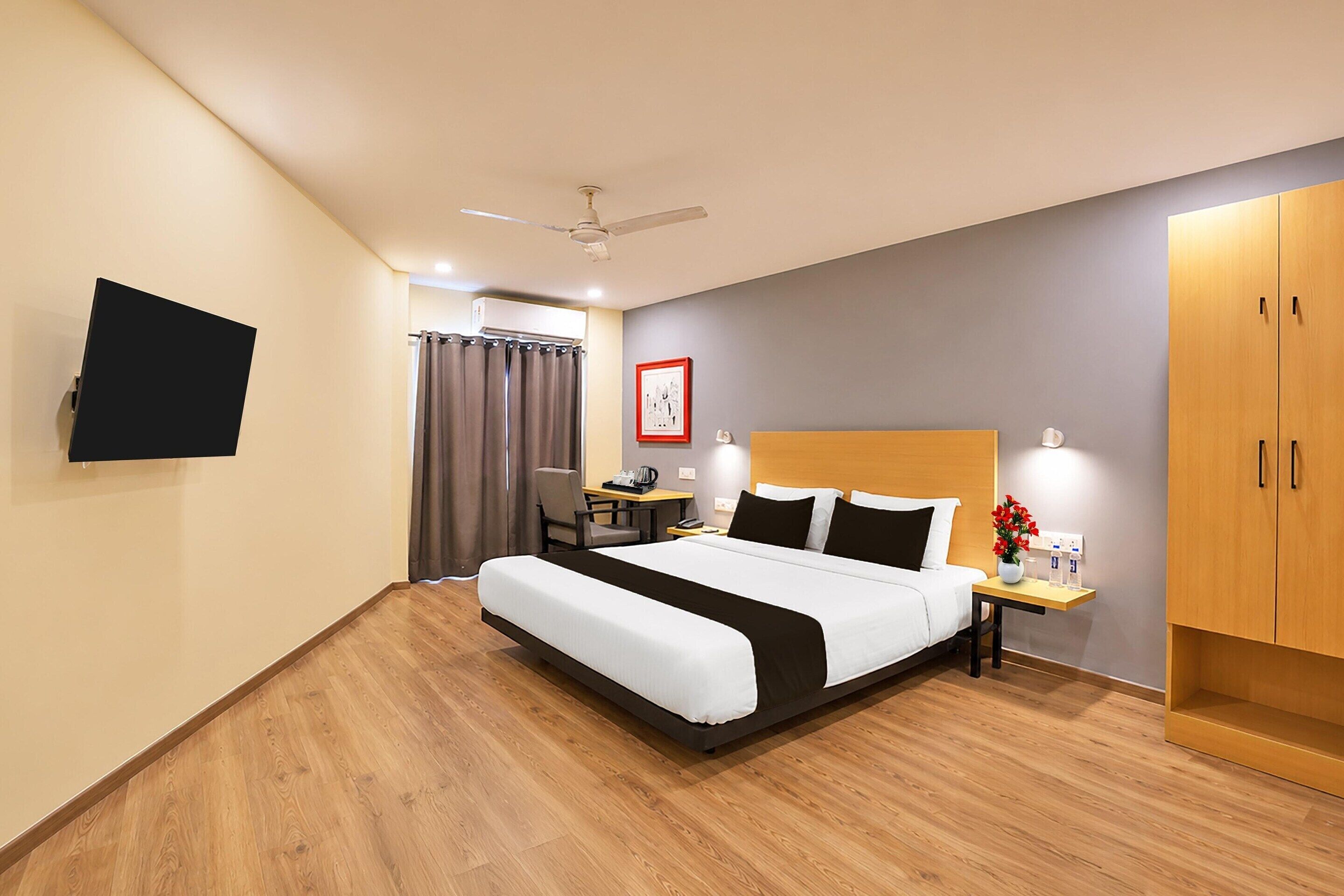 Habitación de hotel con cama, escritorio, silla, televisor, armario y ventilador de techo.