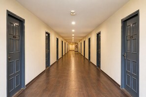 A long, narrow hallway with dark wooden floors and cream-colored walls, leading to multiple doors with numbers. - Classic Neelkanth (Ahmedabad)