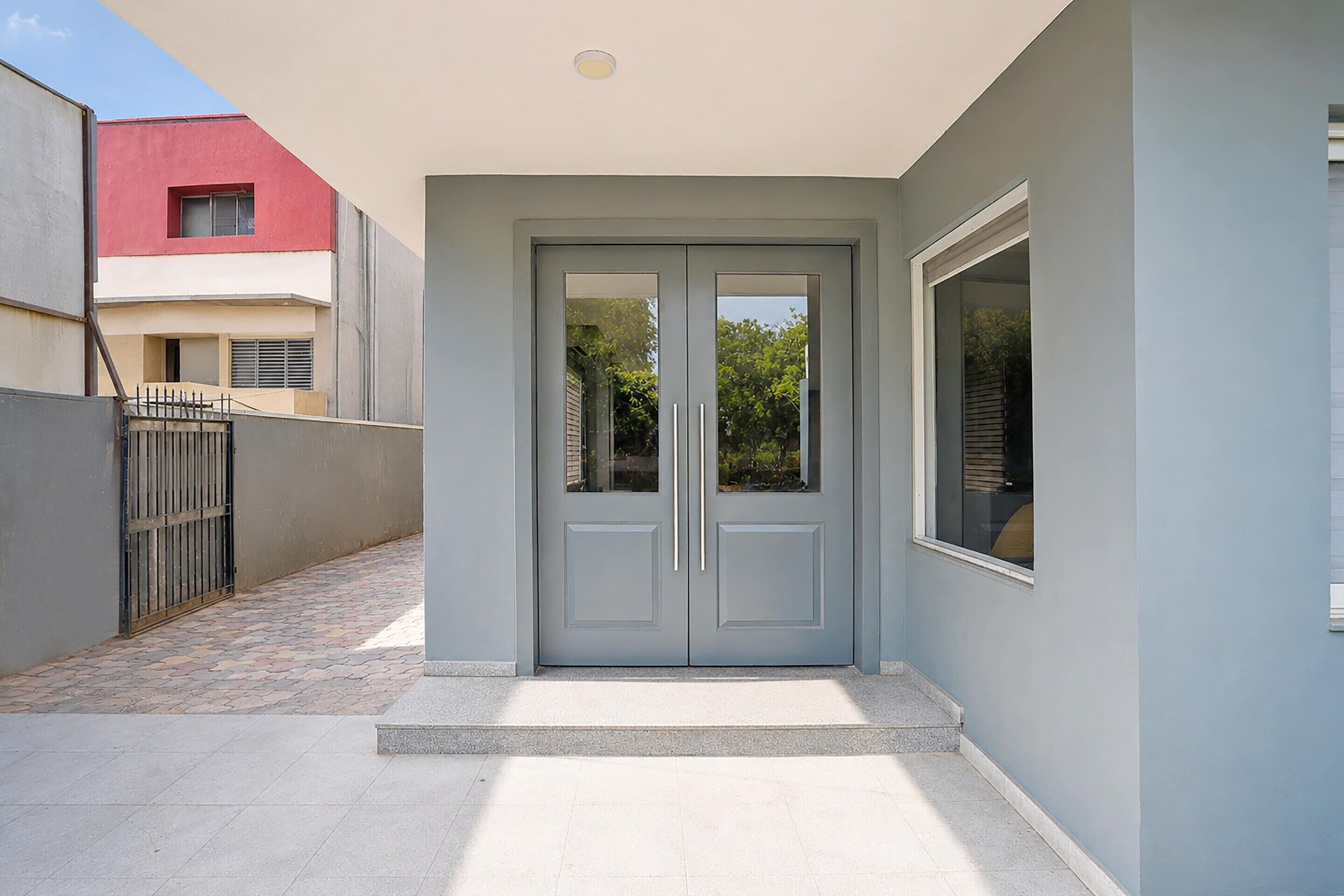 A modern building entrance with a grey door, a small window, and a tiled pathway.