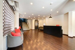 A spacious lobby with a reception desk, a staircase, and a seating area with a sofa and cushions. - Classic Neelkanth (Ahmedabad)