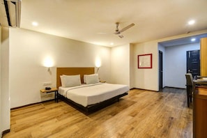 Quarto de hotel com cama, mesa de cabeceira, ventilador de teto e piso de madeira.
