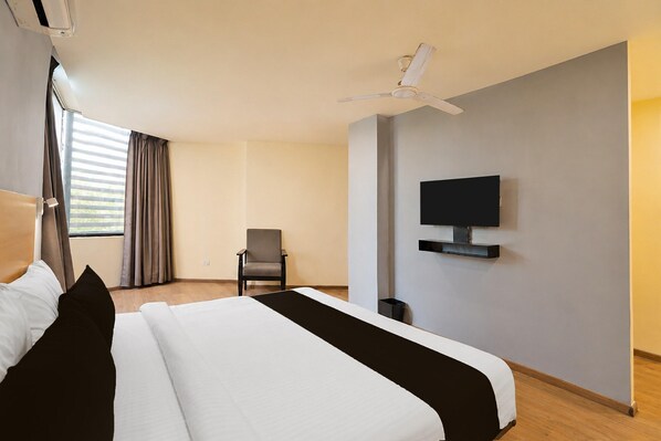 A hotel room with a bed, a chair, a TV mounted on the wall, and a ceiling fan.