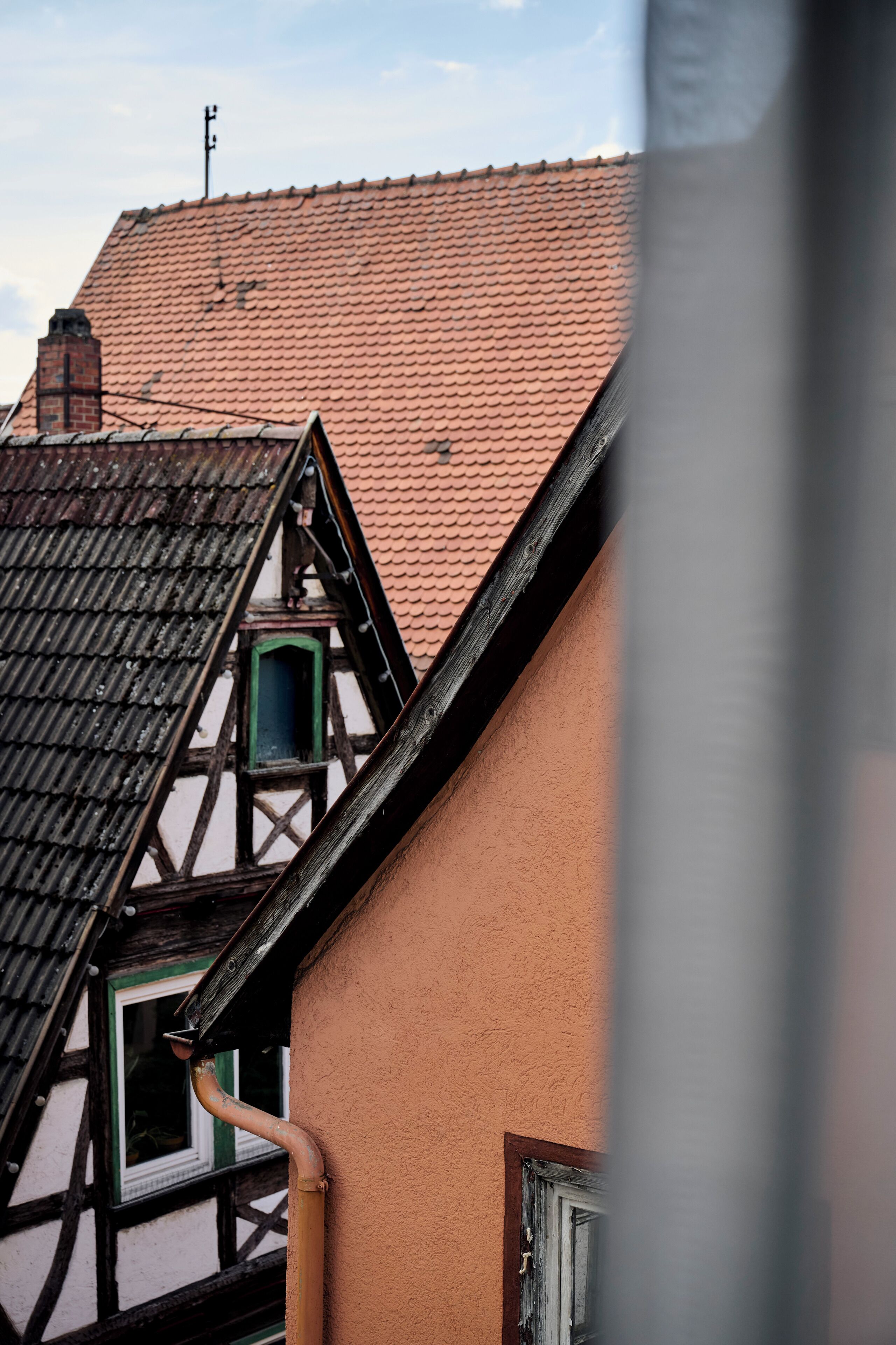 A traditional half-timbered building with a steeply pitched roof, a visible chimney, and a window with a green frame.