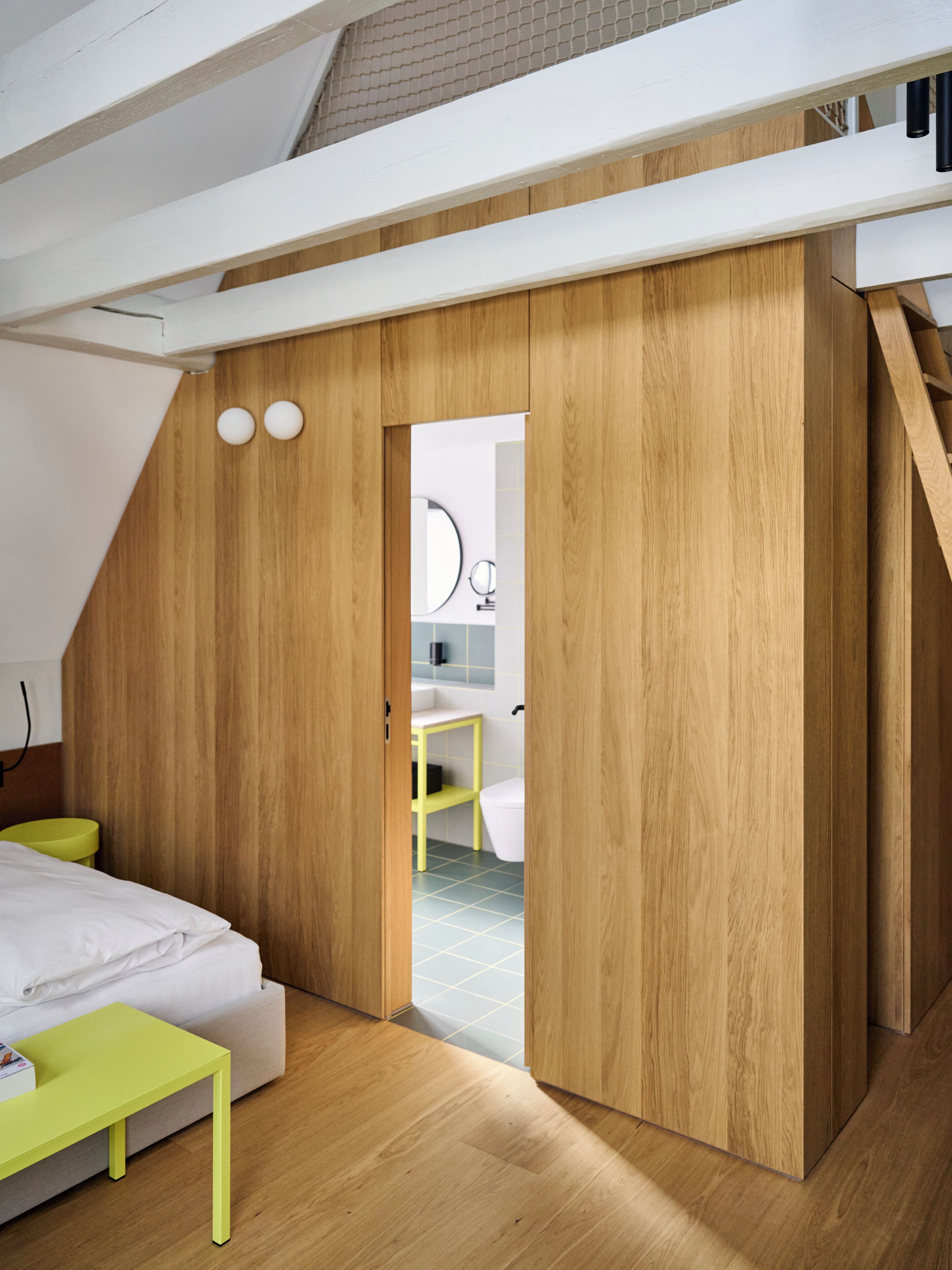 Une chambre à coucher avec un lit, une table verte, des murs en bois et une salle de bain visible à travers une porte ouverte.