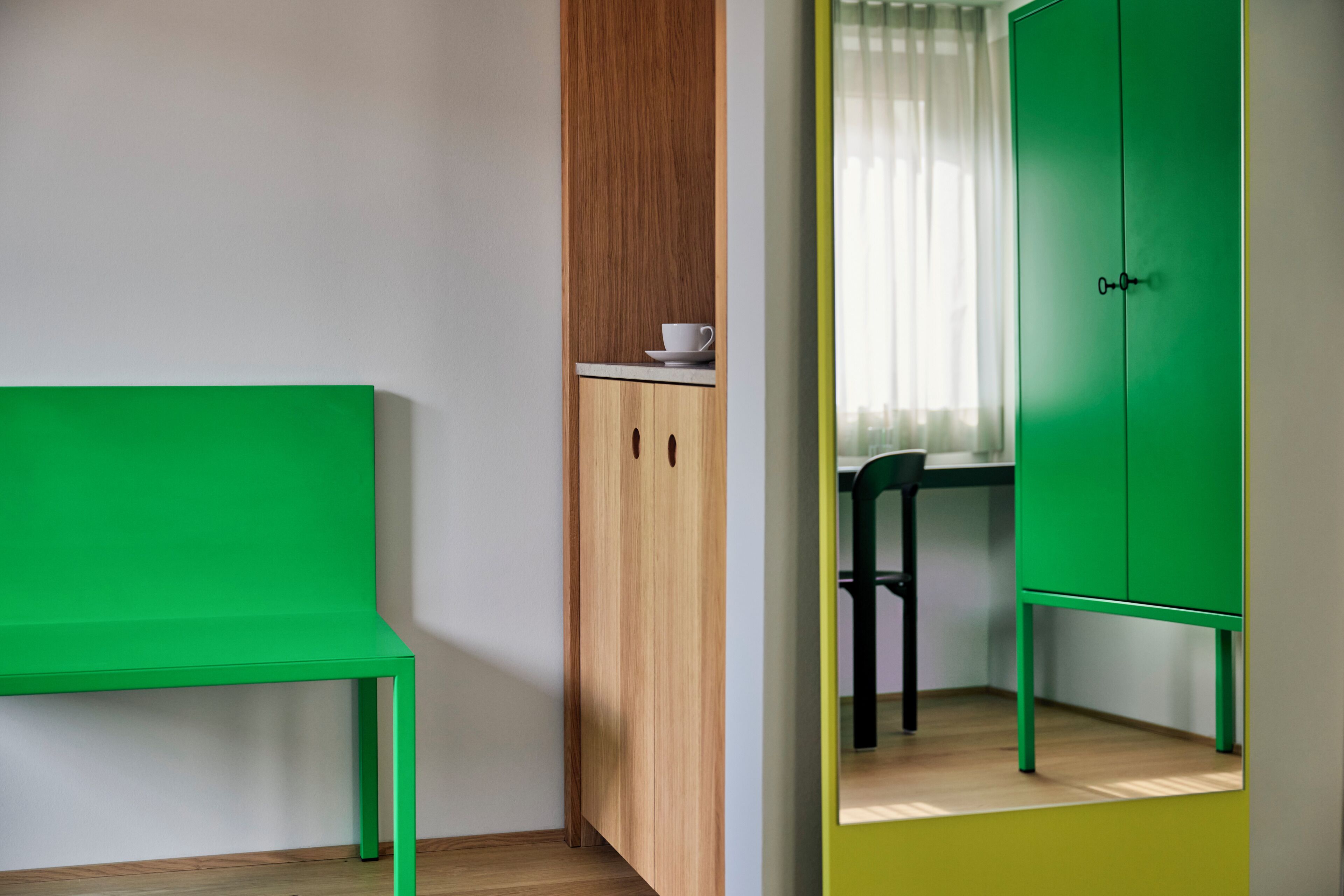 A room with a green bench, wooden cabinets, and a green wardrobe.