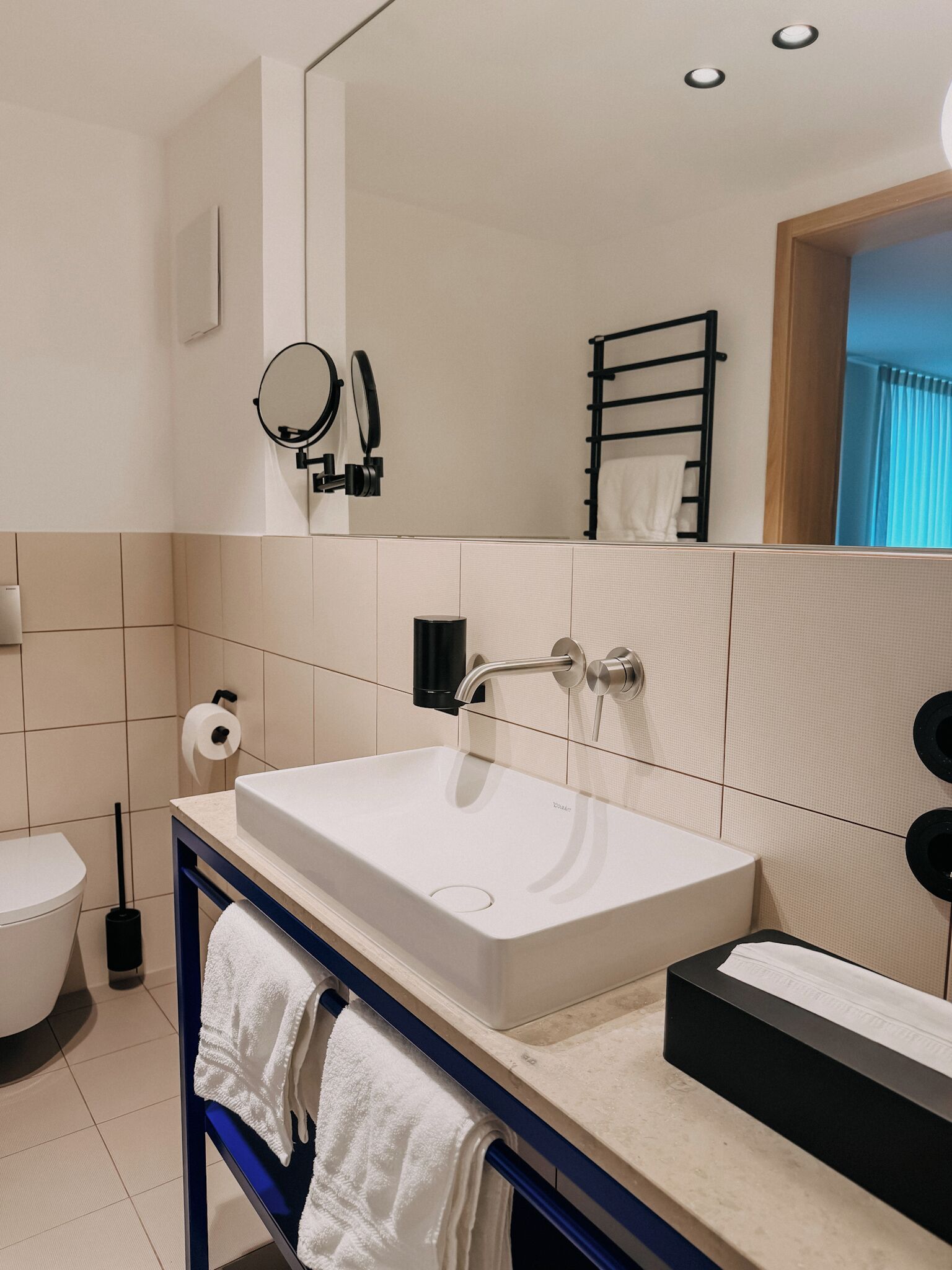 A modern bathroom with a white sink, a mirror, a towel rack, and a toilet.