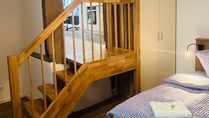 A bedroom with a wooden staircase, a bed with checkered bedding, a wardrobe, and a hanging light fixture. - Exceptional apartment in a historic building with a view of the garden. (Bad Iburg)