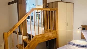 Ein Schlafzimmer mit einer Holztreppe, einem Bett mit karierter Bettwäsche, einem Kleiderschrank und einer Hängeleuchte.