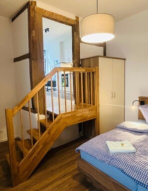 Ein Schlafzimmer mit einer Holztreppe, einem Bett mit karierter Bettwäsche, einem Kleiderschrank und einer Hängeleuchte.