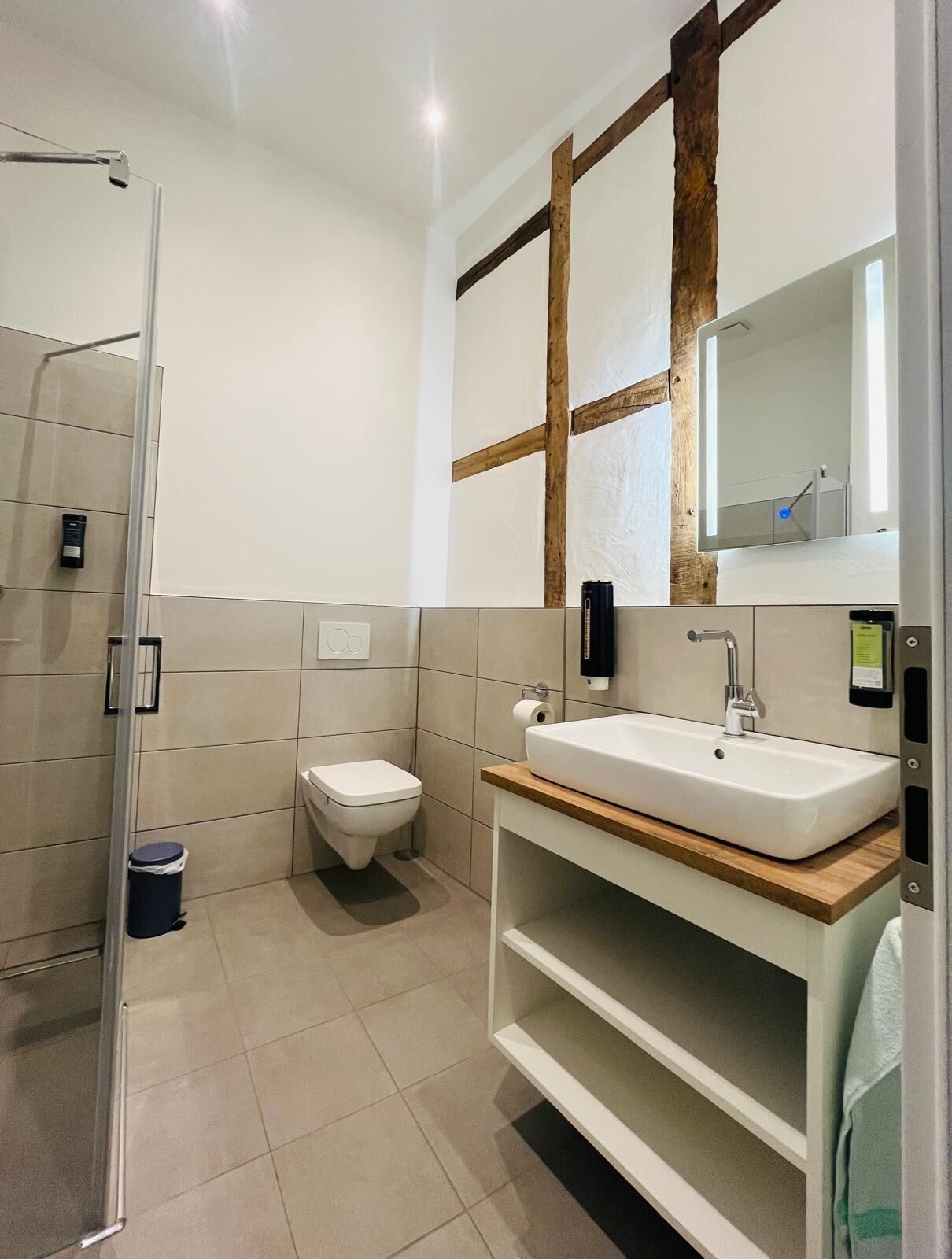 Ein modernes Badezimmer mit Glasdusche, Toilette, Waschbecken mit Holzablage und großem Spiegel mit Holzrahmen.