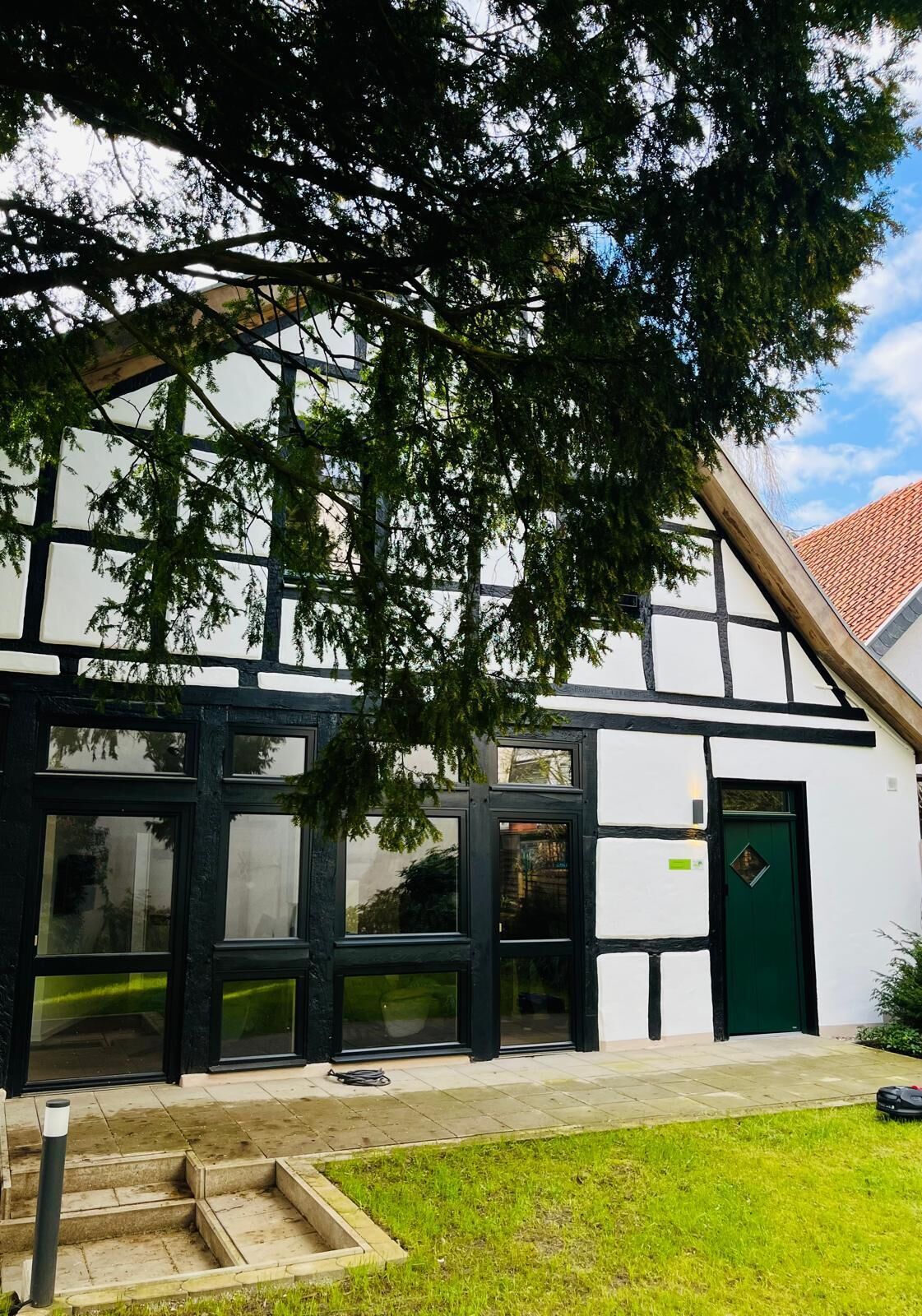 Een traditioneel vakwerkhuis met een groene deur, grote ramen en een boom ervoor.