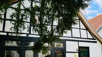 Een traditioneel vakwerkhuis met een groene deur, grote ramen en een boom ervoor.