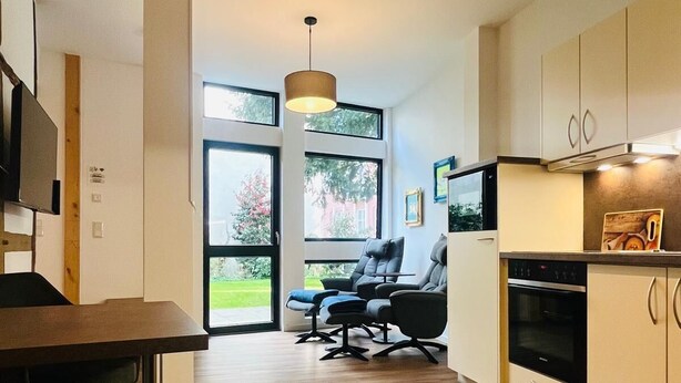 A modern kitchen with wooden flooring, a dining area with a table and chairs, and a seating area with a sofa and chairs. - Exceptional apartment in a historic building with a view of the garden. (Bad Iburg)