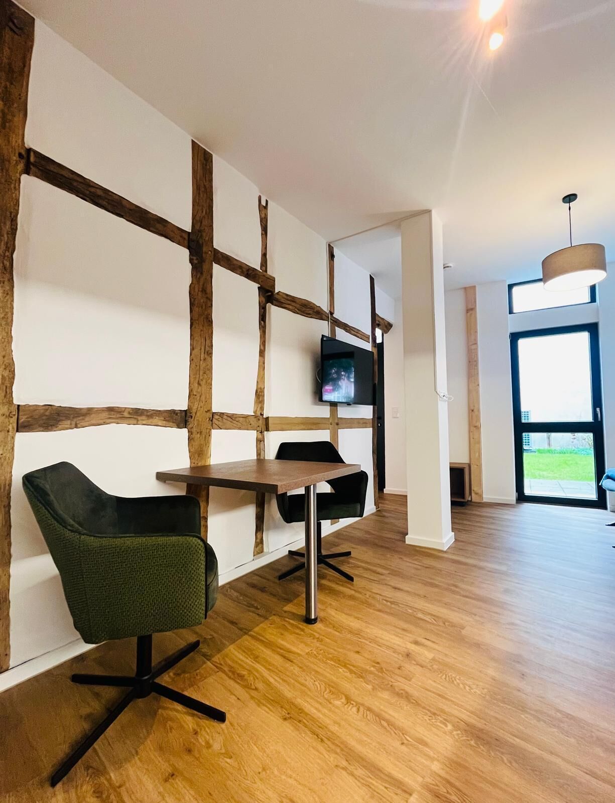 Een modern interieur met een houten accentmuur, een aan de muur bevestigde televisie, een eettafel met stoelen en een groot raam dat natuurlijk licht biedt.