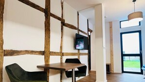 A modern interior with a wooden accent wall, a TV mounted on the wall, a dining table with chairs, and a large window providing natural light. - Exceptional apartment in a historic building with a view of the garden. (Bad Iburg)
