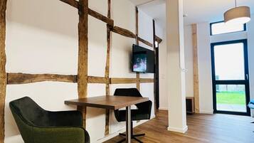 Een modern interieur met een houten accentmuur, een aan de muur bevestigde televisie, een eettafel met stoelen en een groot raam dat natuurlijk licht biedt.