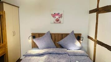 A bedroom with a bed, a hanging light, a wooden headboard, a wall-mounted picture, and a wooden wardrobe.