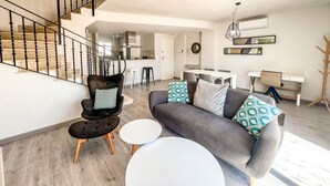 Ein modernes Wohnzimmer mit Treppe, einer Couch mit gemusterten Kissen, einem Essbereich und einem Garderobenständer.