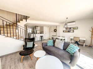 Ein modernes Wohnzimmer mit Treppe, einer Couch mit gemusterten Kissen, einem Essbereich und einem Garderobenständer.