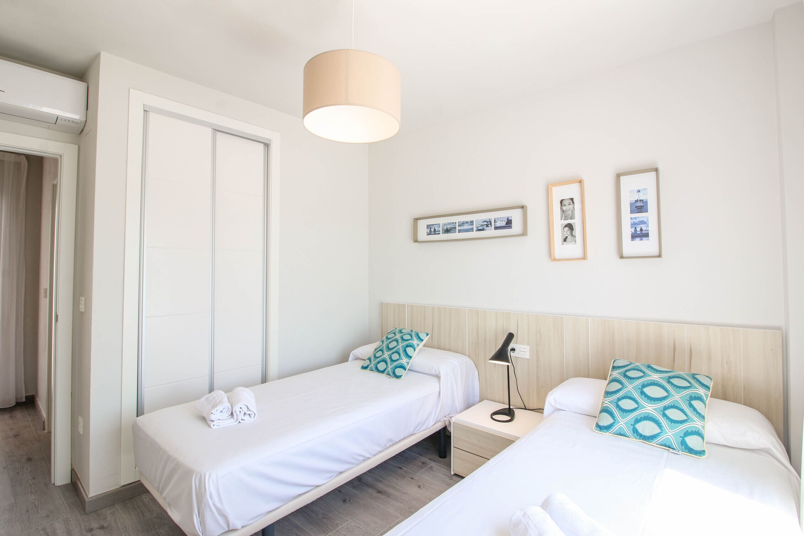 Ein Hotelzimmer mit zwei Betten, einem Nachttisch mit Lampe, einem Kleiderschrank und gerahmten Bildern an der Wand.