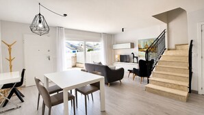 Ein modernes Wohnzimmer mit Essbereich, einer Treppe und Blick ins Freie.