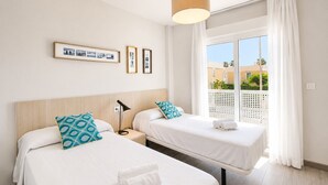 Ein Hotelzimmer mit zwei Betten, einem Nachttisch, einer Lampe, einem Fenster mit Vorhängen und Balkonblick.