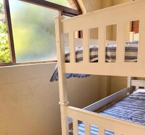 Een stapelbed met strepen gordijnen, een raam met uitzicht op groen, en een effen muur.