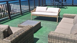 Ein Balkon mit Korbmöbeln, einem Tisch und Blick auf das Meer.