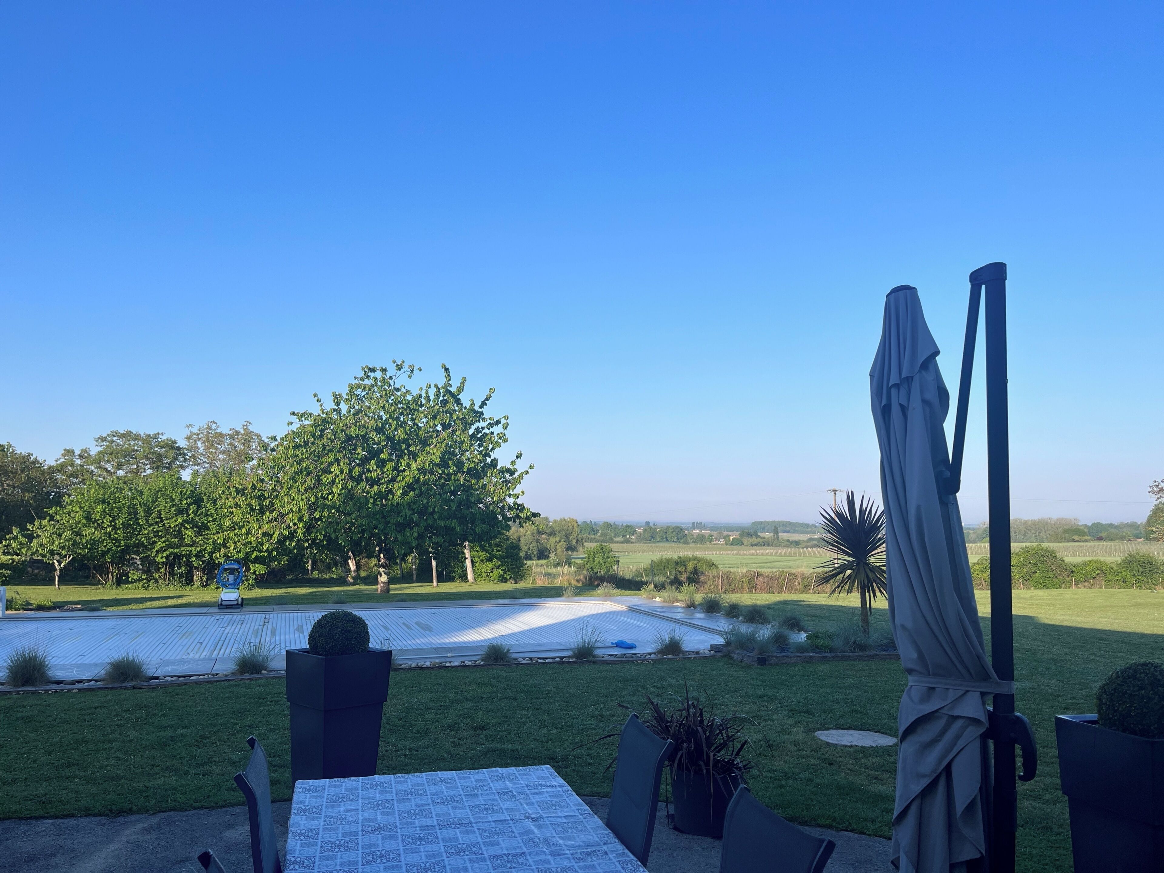 Une terrasse avec une table et des chaises, un parasol et une vue sur un champ et des arbres.