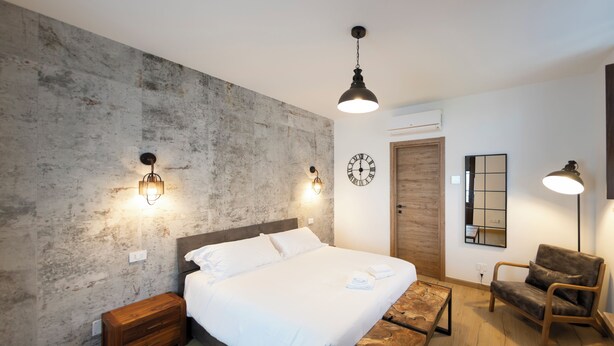 A bedroom with a bed, bedside tables, a wooden bench, a chair, a clock, and wall-mounted lighting. - New TENUTA MARELLA Farmstay, nestled in the countryside just outside Rome (Lazio)
