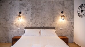 A neatly made bed with white linens and towels, two wall-mounted light fixtures, a wooden nightstand, and a clock on the wall. - New TENUTA MARELLA Farmstay, nestled in the countryside just outside Rome (Lazio)