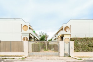 A gated entrance to a residential building with a flat facade, circular windows, and a hedge on the right. - Casa Eos (Torre A Mare)
