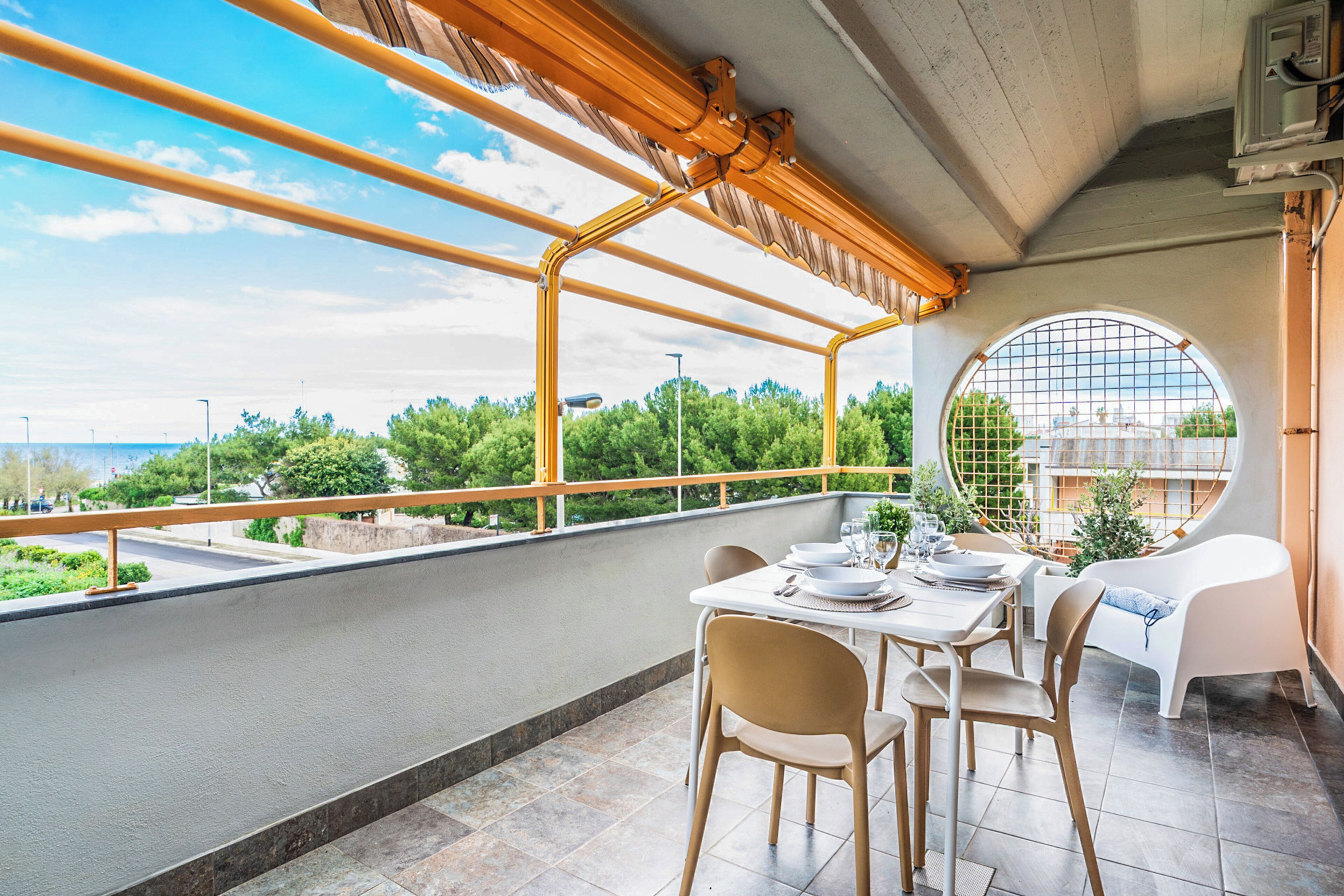 Un balcón con mesa lista para comer, una silla y vistas a zonas verdes y edificios.