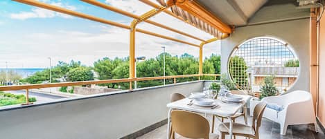 Un balcón con mesa lista para comer, una silla y vistas a zonas verdes y edificios.