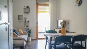 A modern living room with a sofa, dining table, chairs, a potted plant, and a TV. - Casa Eos (Torre A Mare)