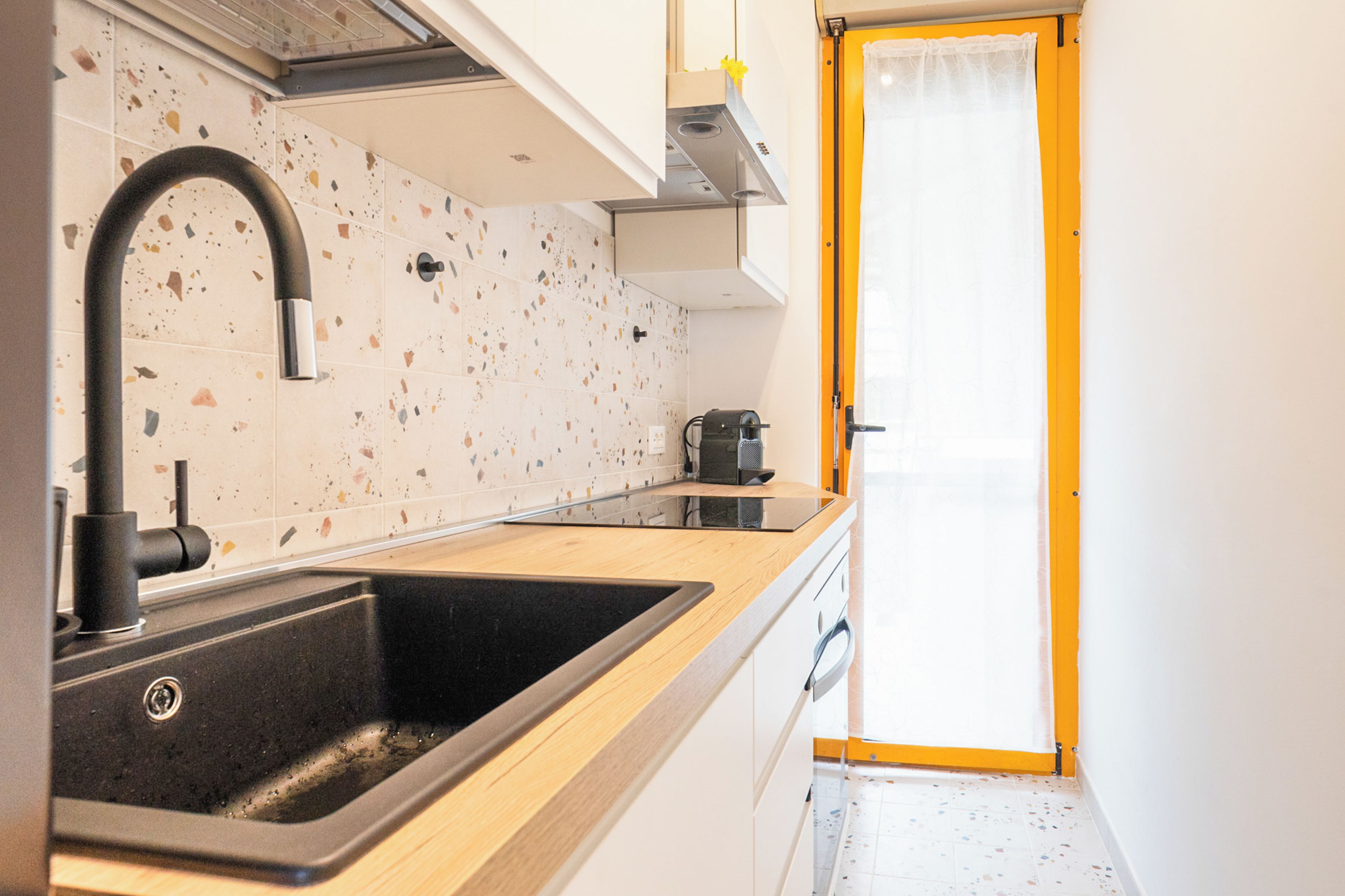 A compact kitchen with a sink, a coffee machine, and a door leading to another room.