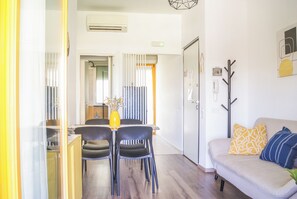 A modern living room with a sofa, a dining table with chairs, and a coat rack. - Casa Eos (Torre A Mare)