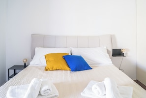 A neatly made bed with a headboard, two pillows, and two rolled towels. - Casa Eos (Torre A Mare)