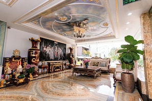 Eine luxuriöse Lobby mit einem prunkvollen Kronleuchter, einem großen Gemälde, aufwendigen Möbeln und einem Marmorboden.