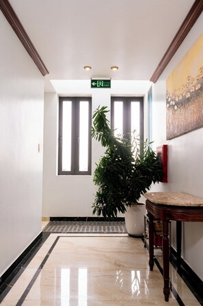 A hallway with a potted plant, a table, and a door with an exit sign. - The Eastern Hotel CatBi Airport (Hai Phong)