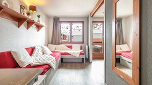 Et hyggeligt rum med en rød sofa, en hvid stol, et lille bord, et spejl og et vindue med gardiner.