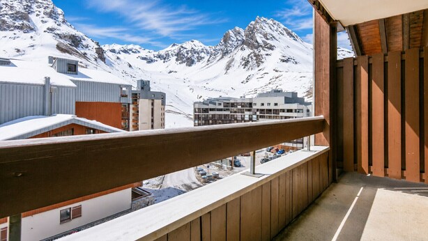 En balkon med trægelænder med udsigt over et sneklædt bjerglandskab og bygninger.