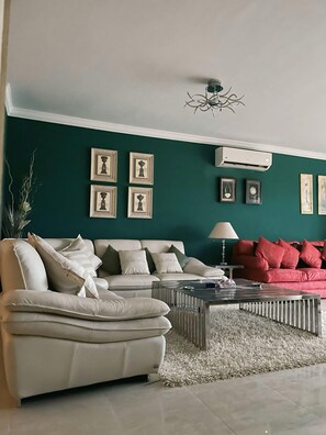 A living room with a beige sofa, a red sofa, a coffee table, and framed pictures on the wall.