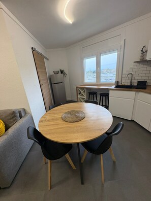 A compact kitchen with a round wooden table, black chairs, a refrigerator, and a window with a view. - Apartment with canal view Empuriabrava (Empuriabrava)