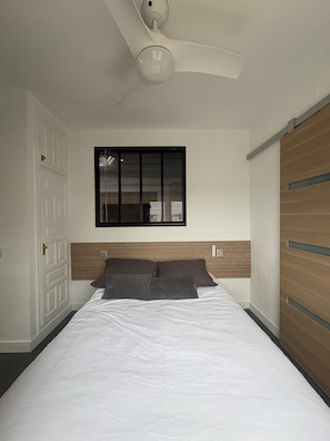 A bedroom with a bed, a ceiling fan, a window with blinds, a door, and a wardrobe. - Apartment with canal view Empuriabrava (Empuriabrava)